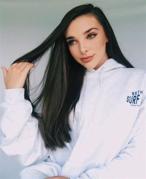 A Woman With Long Black Hair Wearing A White Hoodie And Posing For The