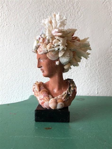 A Statue Of A Woman With Seashells On It S Head Is Sitting On A Green Table