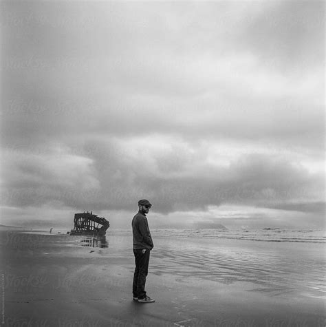 Man Standing On The Beach With A Shipwreck In Black And White Del