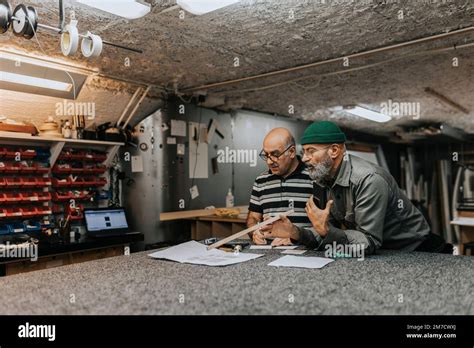 Mature Craftsman Discussing Over Blueprint With Male Colleague At
