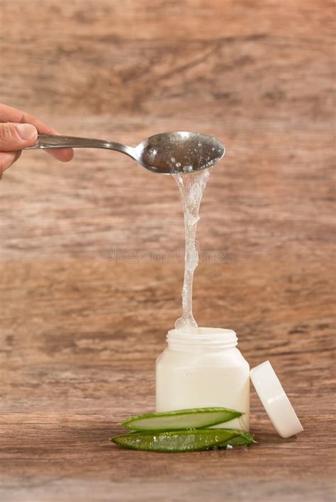 Person Placing Aloe Vera Pulp In A Plastic Container With A Metal Spoon