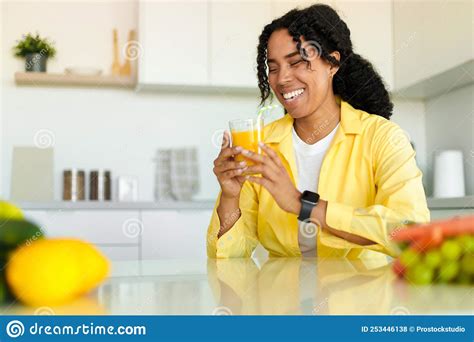 Excited Black Lady Drinking Fresh Orange Juice At Home Sitting At