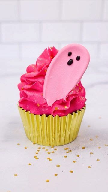 A Cupcake With Pink Frosting And A Ghost Face On Its Side