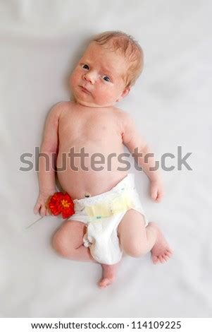 Tiny Naked Newborn Baby In Diapers Holding Orange Flower Of Garden