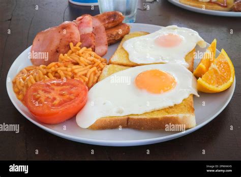 Australian Breakfast With Fried Eggs On Toast Bacon Sausages Spaghetti Tomato And Orange