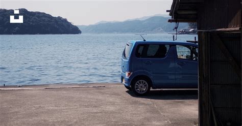 A Small Blue Van Parked Next To A Large Body Of Water Photo Free