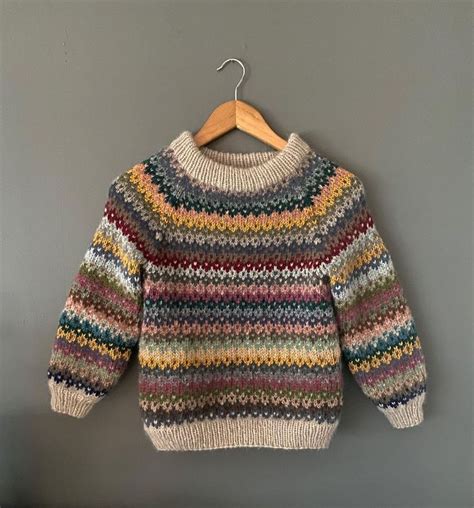 A Multicolored Sweater Hangs On A Hanger Against A Gray Wall With A