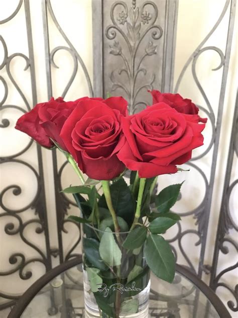 Three Red Roses In A Clear Vase On A Glass Table With Wrought Ironwork