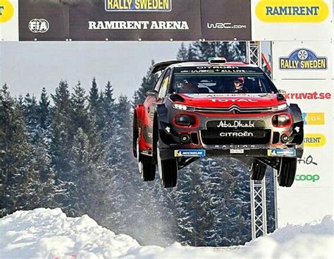 A Red Car Is Jumping In The Air Over Snow Covered Ground With Trees