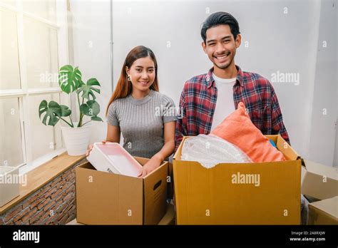 Asian Young Couple Carrying Big Cardboard Box For Moving In New House