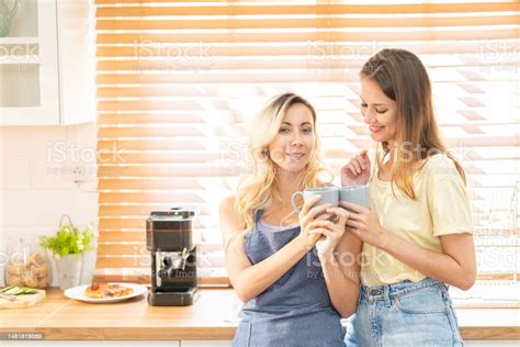 Happy Lesbian Couple Holding Cups Of Coffee In Kitchen Couple Of