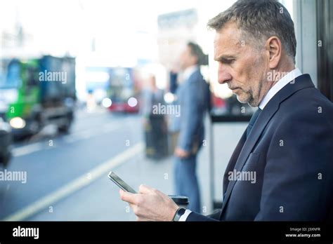 Businessman Waiting At Bus Stop Using Smartphone London Uk Stock