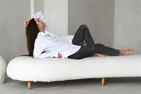 Beautiful Brunette Posing In Studio While Lying On A White Sofa Beautiful Brunette Looks Away