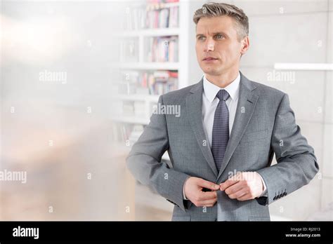 Confident Mature Salesman Looking Away While Buttoning Suit Against