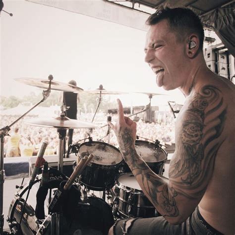 A Man With Tattoos On His Arm Playing Drums In Front Of A Large Group