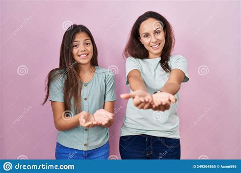 Young Mother And Daughter Standing Over Pink Background Smiling With