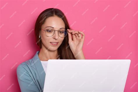 Портрет крупного плана очаровательной дамы касаясь рамке ее Eyeglasses с рукой и смотря экран