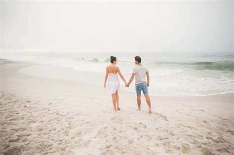 Vista traseira do casal de mãos dadas e caminhando na praia Foto Premium