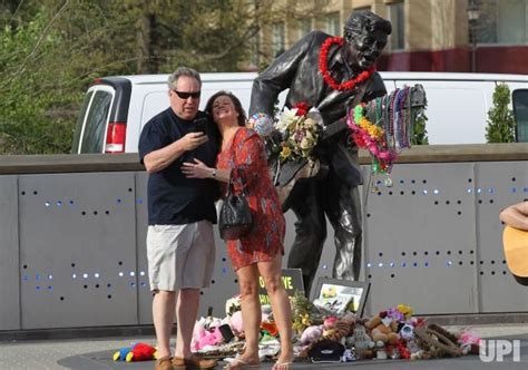 A Woman Standing Next To A Statue With Flowers On It And People Looking