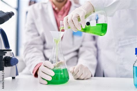 Man And Woman Wearing Scientists Uniform Pouring Liquid On Test Tube At