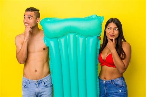 Joven pareja latina sosteniendo colchón de aire aislado sobre fondo amarillo mirando hacia los