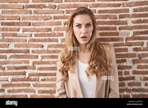 Beautiful Blonde Woman Standing Over Bricks Wall Afraid And Shocked