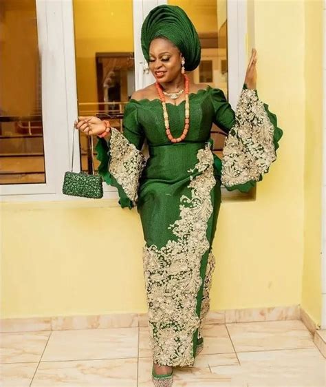 A Woman In A Green And Gold Dress Is Standing By A Window With Her Hand