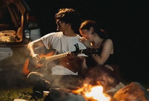 A Man And Woman Sitting Next To Each Other On The Ground With A Guitar