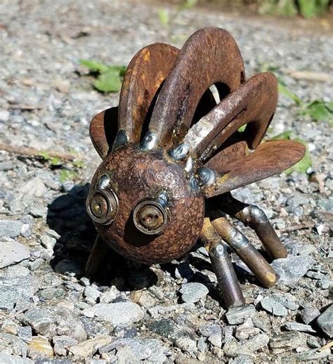 A Small Metal Insect Sitting On Top Of A Gravel Road Next To Grass And