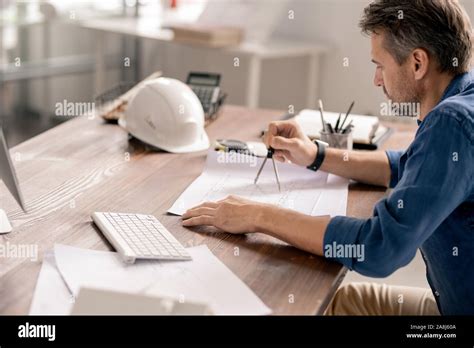 Serious Mature Engineer In Casualwear Using Dividers While Drawing