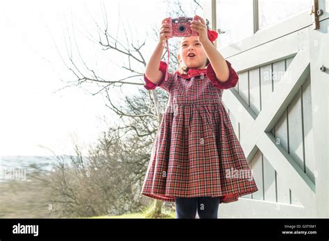 A Six Year Old Girl Standing At A Back Door Taking Pictures With A Toy