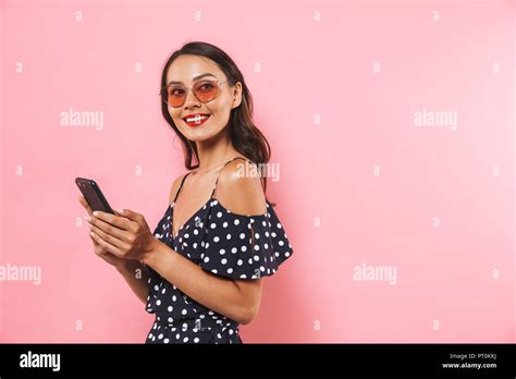 Side View Of Smiling Brunette Woman In Dress And Sunglasses Holding Smartphone While Looking At
