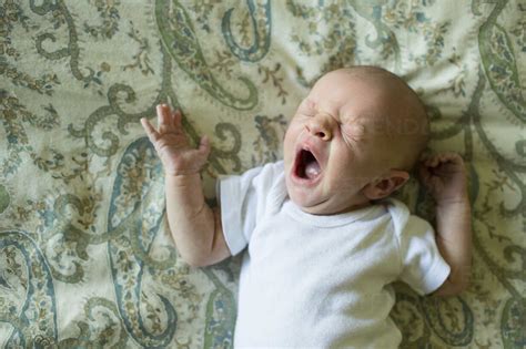 High Angle View Of Baby Boy Yawning While Sleeping On Bed At Home Stock