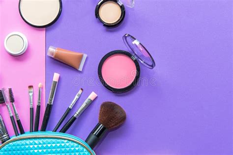 A Blue Cosmetics Bag With Makeup Products Spilling Out On To A Pastel Pink Background Stock