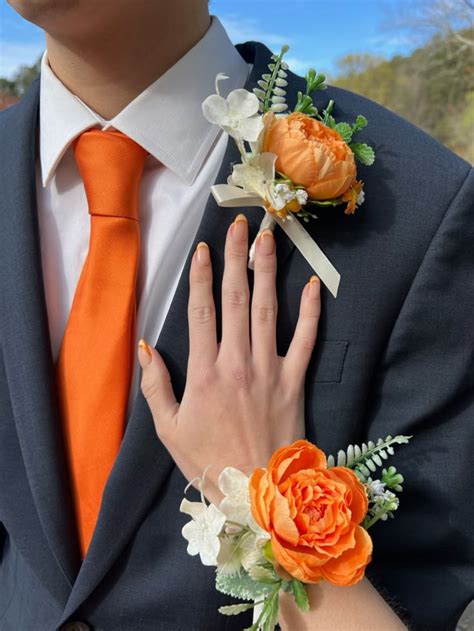 A Man Wearing An Orange Tie And Matching Boutonniere Is Holding His