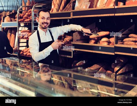 Positive Male Shop Assistant Demonstrating Delicious Loaves Of Bread In