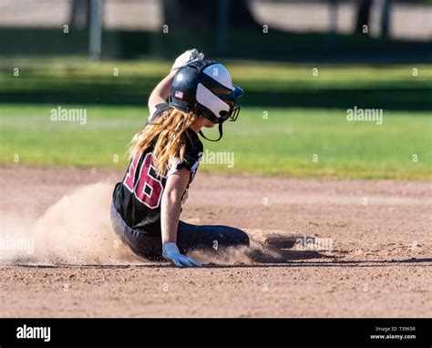 Female Teenage Softball Player In Black Uniform Sliding Safely Into