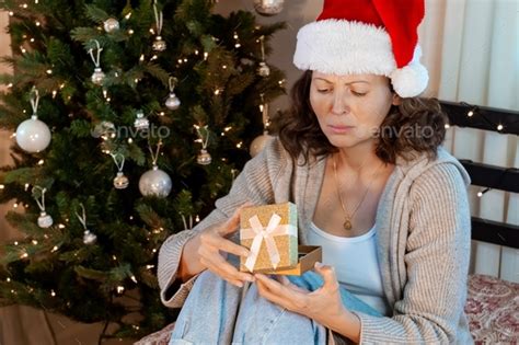 Grumpy Unhappy Woman Is Sitting Next To Christmas Tree With Gift Stock