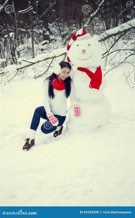 A Menina Moreno No Chapéu E Nos Mitenes Esculpe Um Boneco De Neve Foto