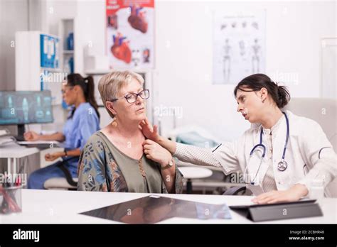 Doctor In Hospital Cabinet Examining Neck Glands Of Senior Patient