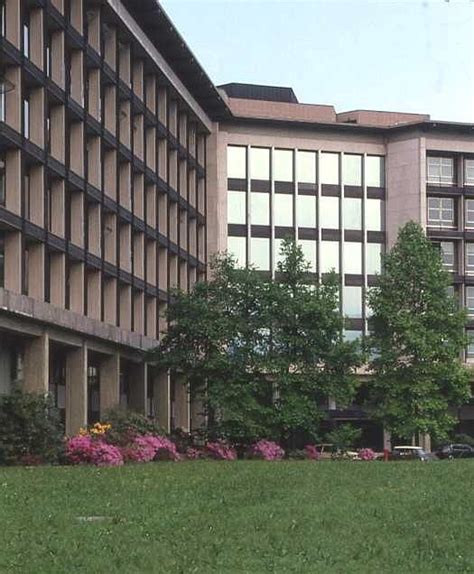 a large building sitting next to a lush green park filled with pink and yellow flowers