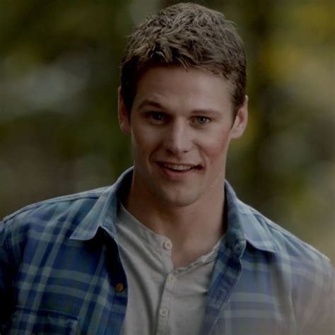 A Young Man Smiling At The Camera With Trees In The Backgrouds Behind Him