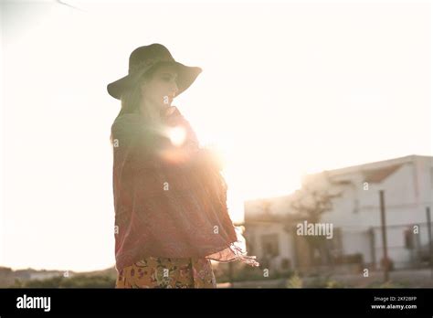 Caucasian Mature Woman With Pink Shawl And Big Red Hat Looking Down At The Backlit Ground On A