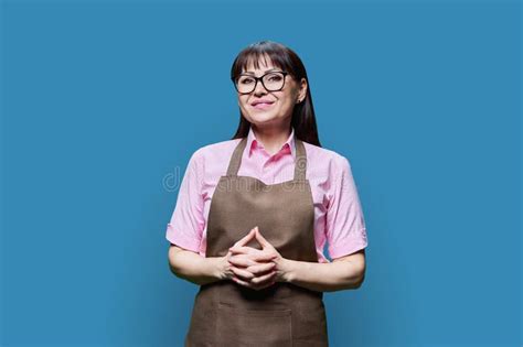 Positive Smiling Mature Woman In Apron On Blue Studio Background Stock