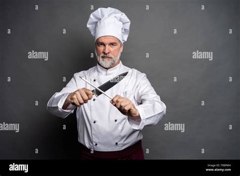 Portrait Of A Mature Chef Cook Holding Knifes Isolated On A Black