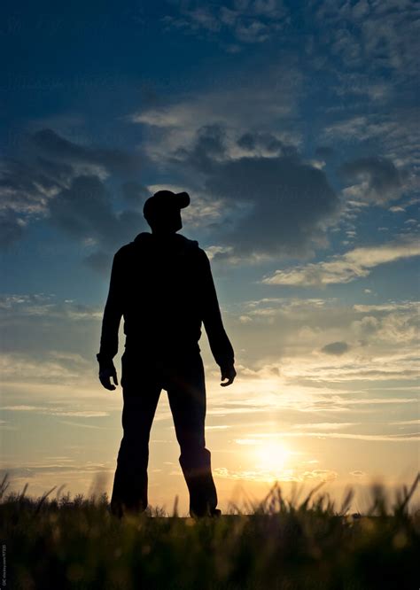 Silhouette Of Man Standing In A Field At Sunset By Stocksy