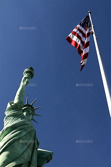 Vertical Image Of The Statue Of Liberty And An American Flag Against A