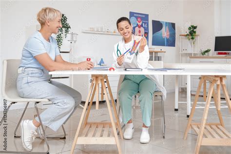 Female Endocrinologist Showing Thyroid Gland Model To Mature Woman At