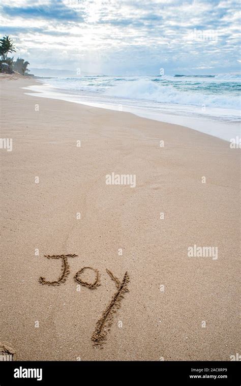 The Word Joy Written In The Sand On The Beach With A Wave Washing In