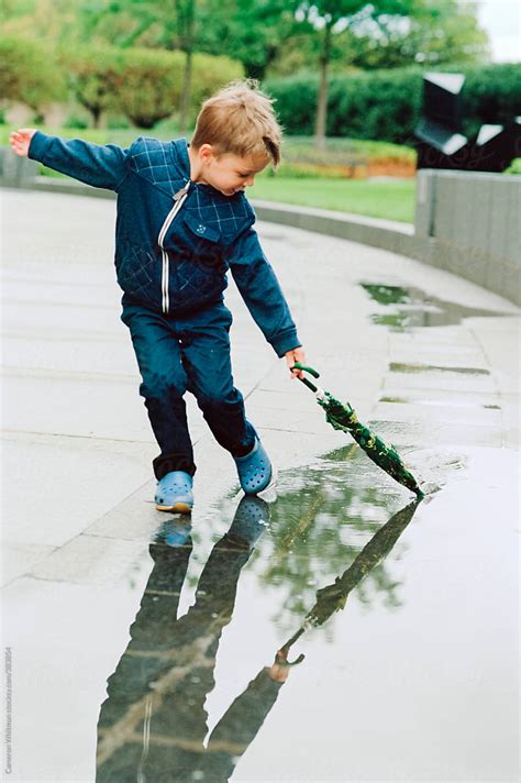 Young Boy Drags His Umbrella Through A Puddle Of Rain Water After A